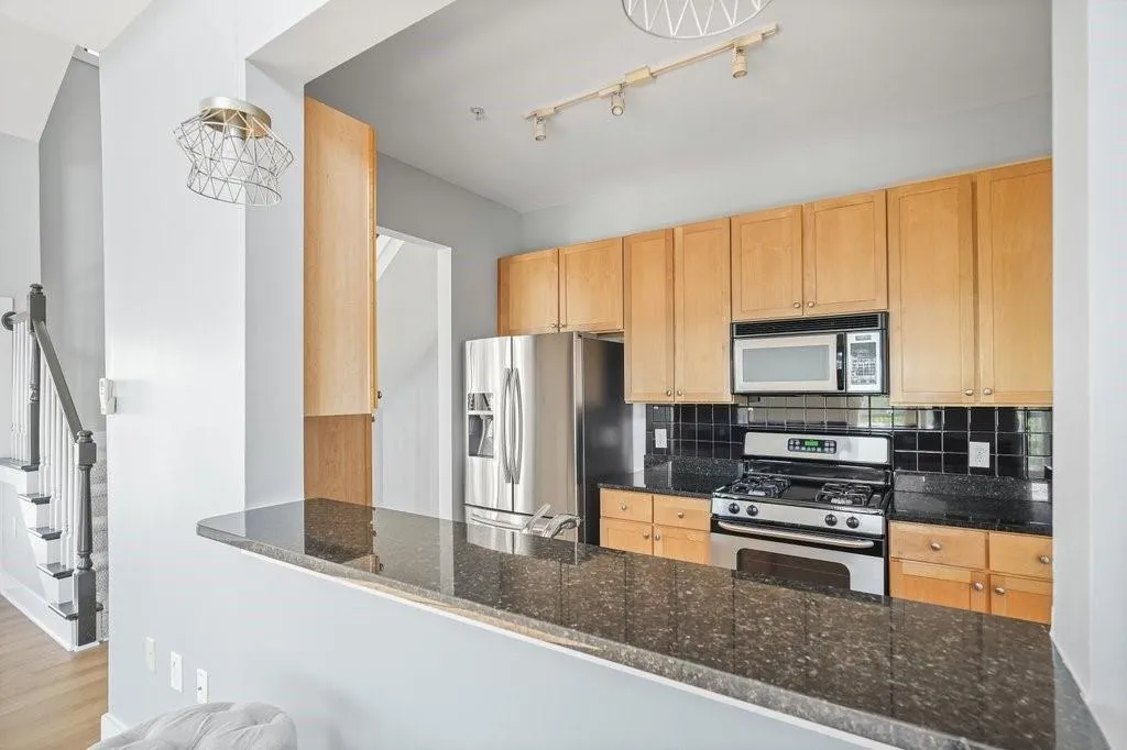 Kitchen with light wood-type flooring, dark stone countertops, stainless steel appliances, rail lighting, and tasteful backsplash Kitchen with light wood-type flooring, dark stone countertops, stainless steel appliances, rail lighting, and tasteful backsplash