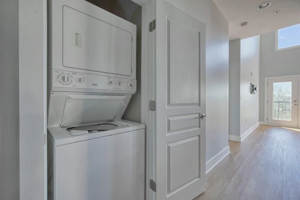 Clothes washing area featuring light hardwood / wood-style floors and stacked washer / drying machine Clothes washing area featuring light hardwood / wood-style floors and stacked washer / drying machine