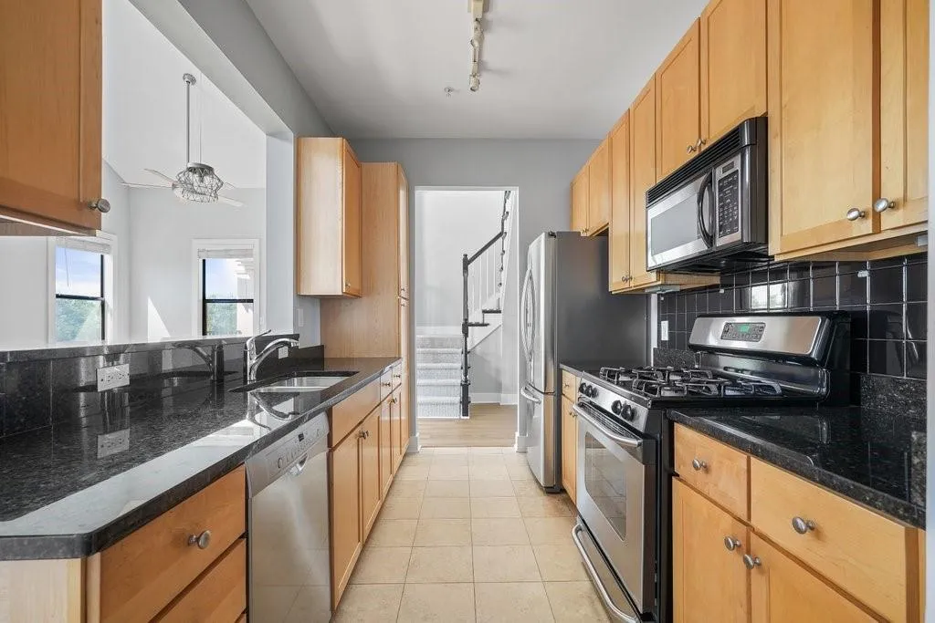 Kitchen with backsplash, track lighting, stainless steel appliances, light tile floors, and dark stone countertops Kitchen with backsplash, track lighting, stainless steel appliances, light tile floors, and dark stone countertops