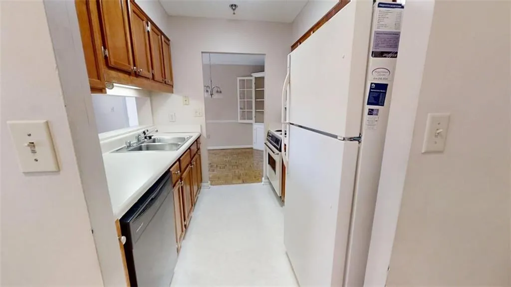 Kitchen with white appliances, brown cabinets, light countertops, light floors, and a sink