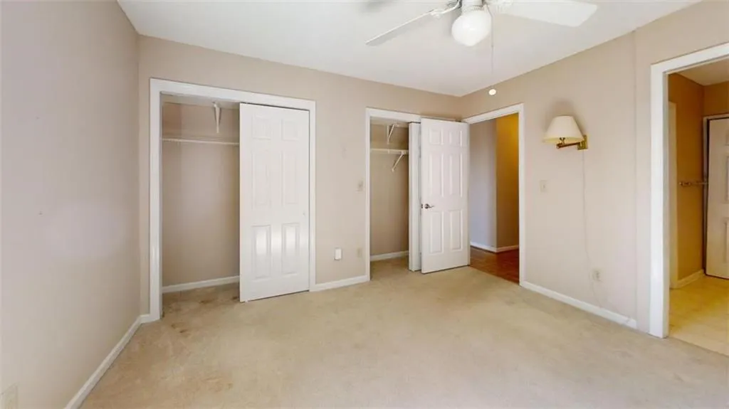 Unfurnished bedroom featuring light carpet, ceiling fan, baseboards, and two closets