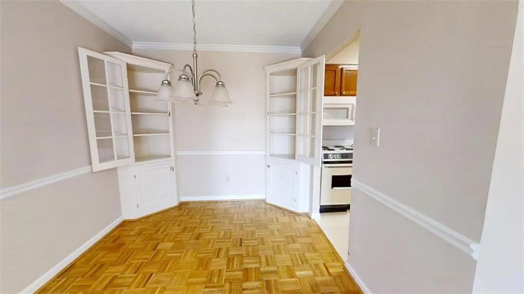 Unfurnished dining area with ornamental molding, a notable chandelier, and baseboards