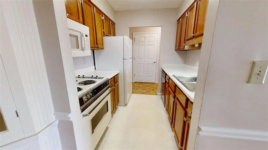 Kitchen featuring white appliances, a sink, light countertops, brown cabinets, and light floors