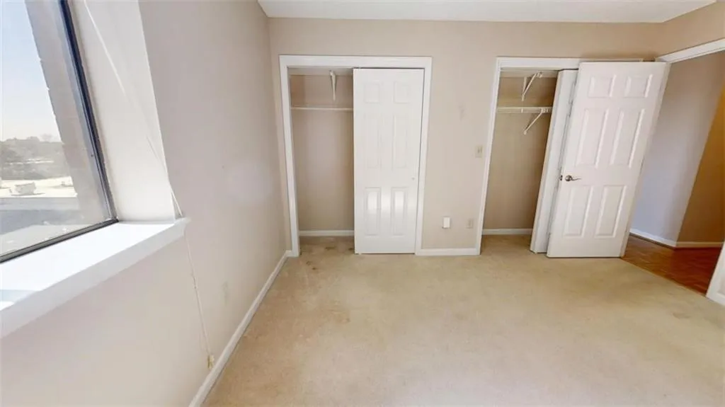 Unfurnished bedroom with multiple closets, light carpet, and baseboards
