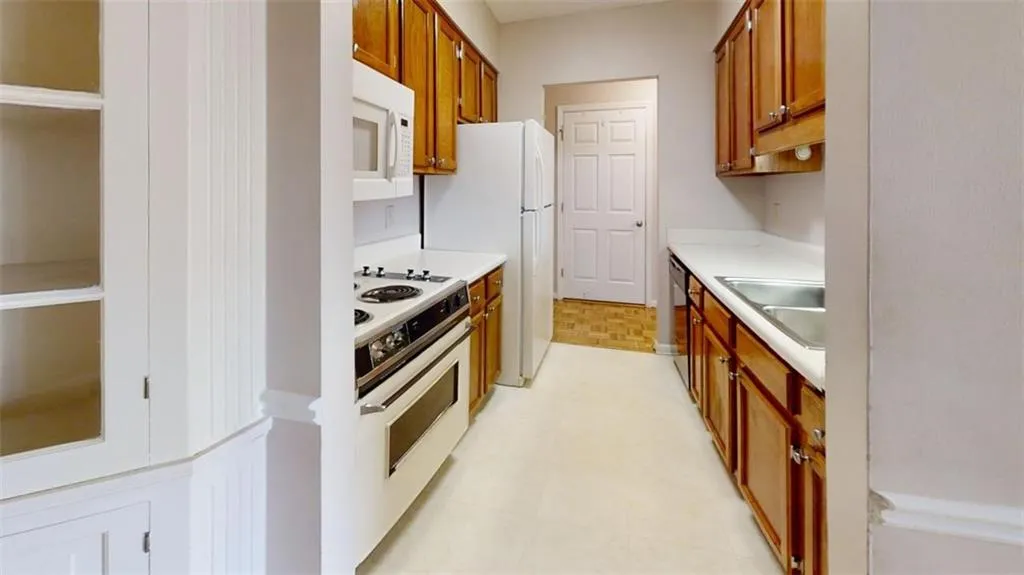 Kitchen with brown cabinets, white appliances, light countertops, and a sink