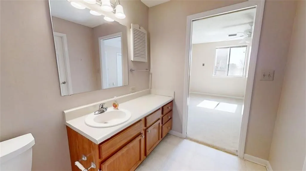 Bathroom with toilet, ceiling fan with notable chandelier, baseboards, and vanity