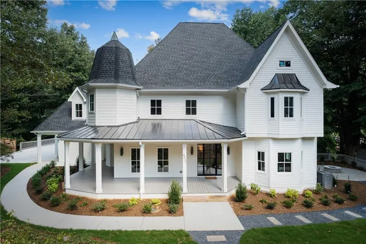 White siding exterior featuring a covered wrap-around porch, turret, metal roof accents, and an integrated bay window