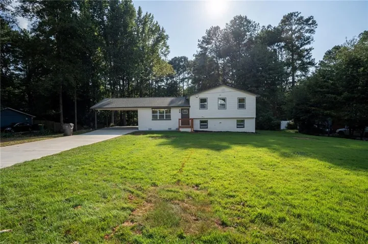 Expansive front lawn, concrete driveway, attached carport, white exterior, and a prominent front door