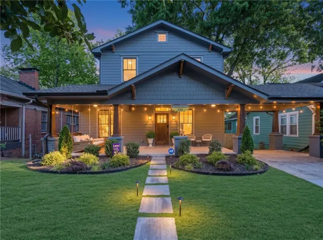 Craftsman-style home featuring a covered front porch with substantial columns, a wood-finish front door, a concrete walkway with integrated lighting, a manicured lawn, and established landscaping