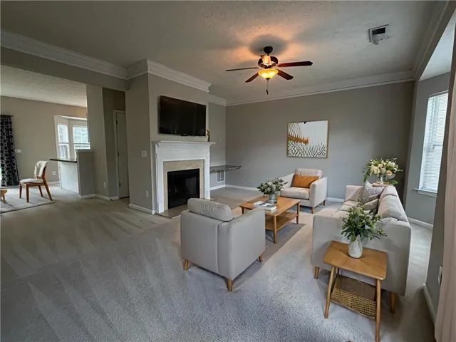 Spacious living room featuring a white-mantled fireplace with a stone surround, crown molding, and a ceiling fan