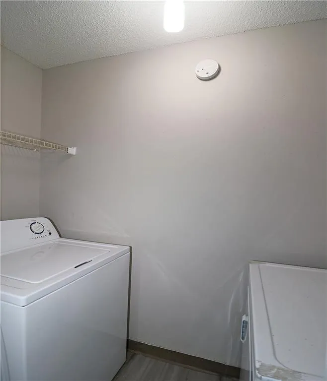 Clothes washing area featuring a textured ceiling, washer / dryer, wood finished floors, and laundry area