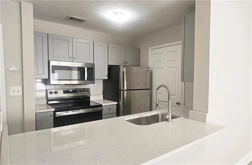 Kitchen with visible vents, light stone counters, gray cabinets, appliances with stainless steel finishes, and a sink