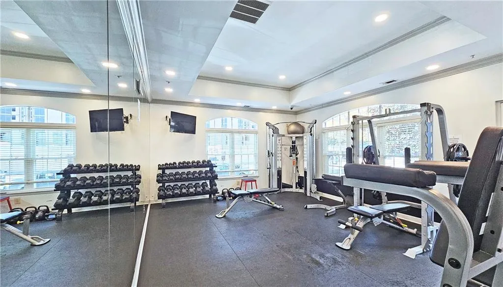 Workout area featuring a tray ceiling, recessed lighting, crown molding, and visible vents