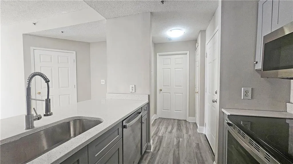 Kitchen featuring light stone countertops, a sink, stainless steel appliances, a textured ceiling, and light wood-type flooring