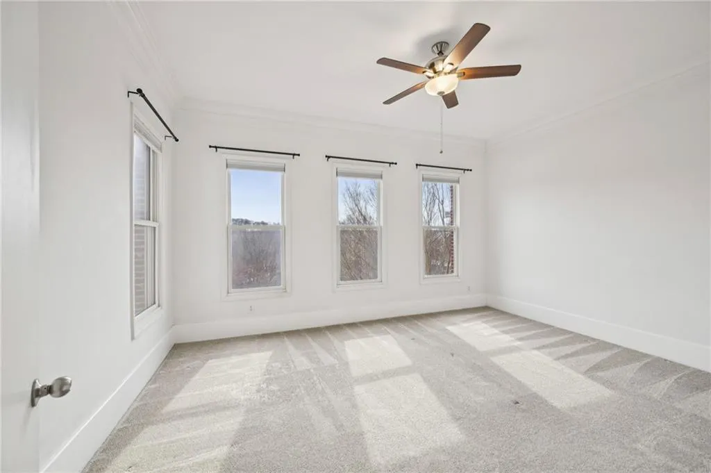 Spacious primary bedroom with plush carpet, ornamental molding, and a ceiling fan. Blinds included!