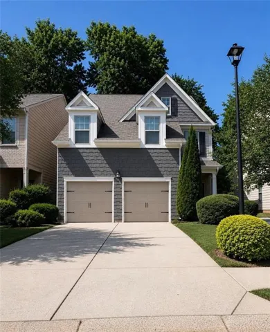 Two-story residence featuring a shingle roof, two dormer windows, and a two-car garage with carriage-style doors