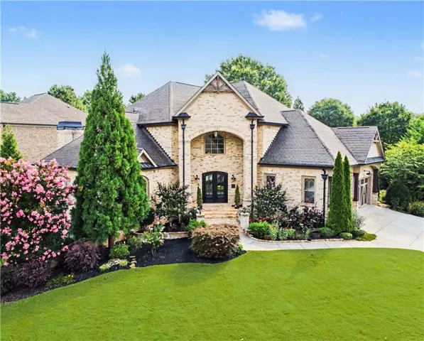 Stone veneer exterior, arched entryway, dark double entry doors, gabled roofline, and established landscaping