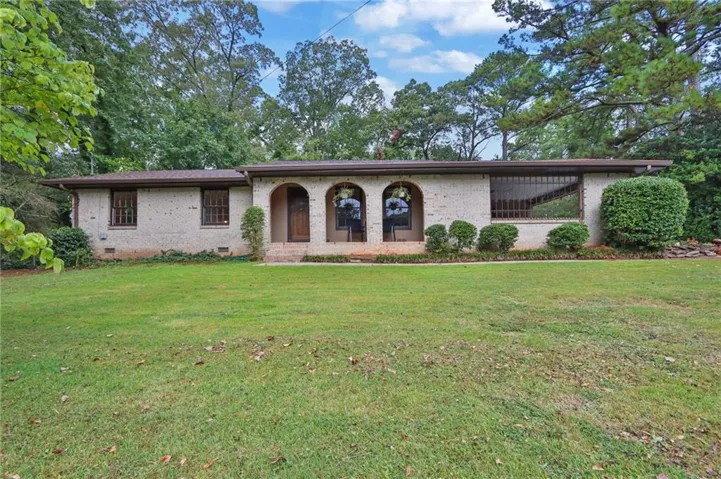 Brick exterior with arched entryways, expansive front lawn, and mature surrounding trees