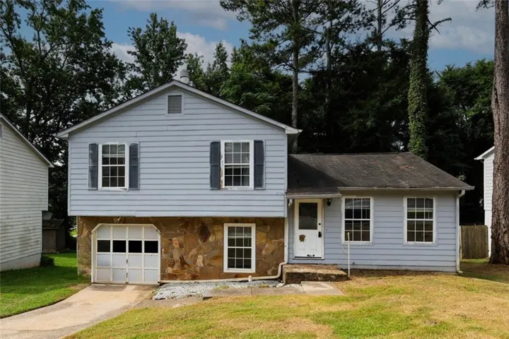 Exterior featuring light blue siding, stone facade, multiple windows with dark shutters, and an attached garage with a panel door