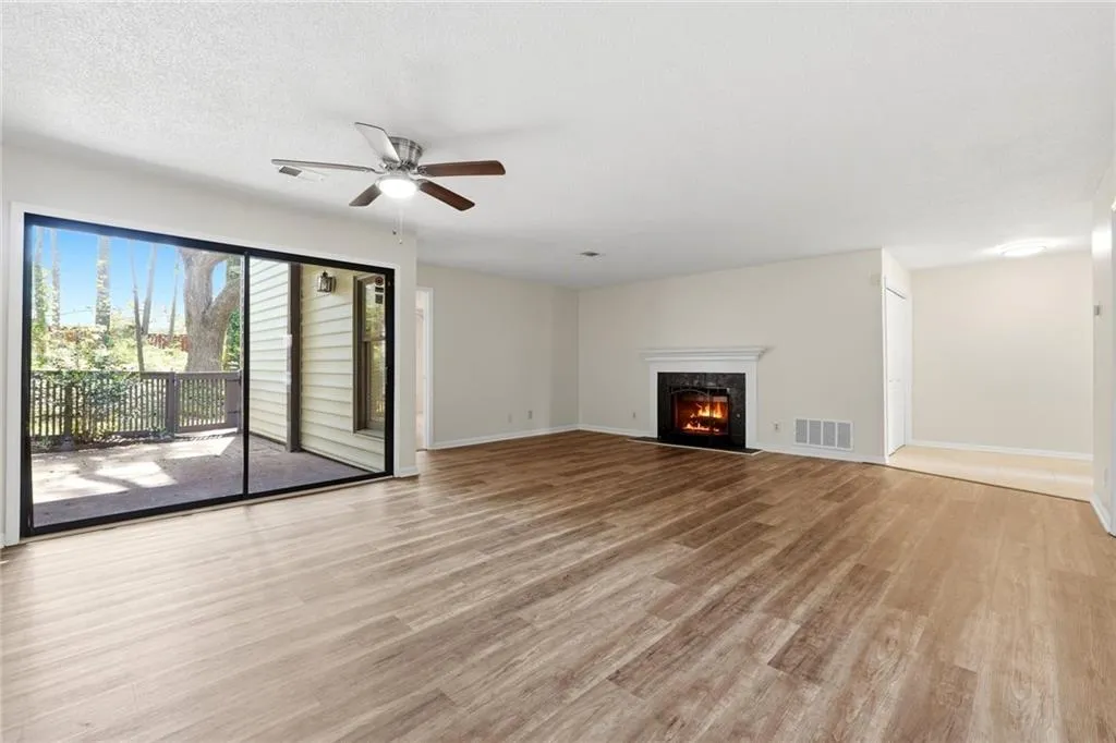 Unfurnished living room with light wood-type flooring, a ceiling fan, a fireplace, and a textured ceiling
