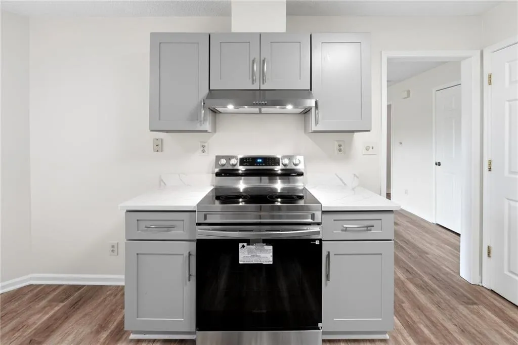 Kitchen with gray cabinets, stainless steel range with electric stovetop, light wood finished floors, and light stone counters