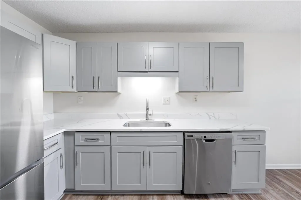 Kitchen featuring stainless steel appliances, gray cabinets, light wood-type flooring, light stone countertops, and a textured ceiling