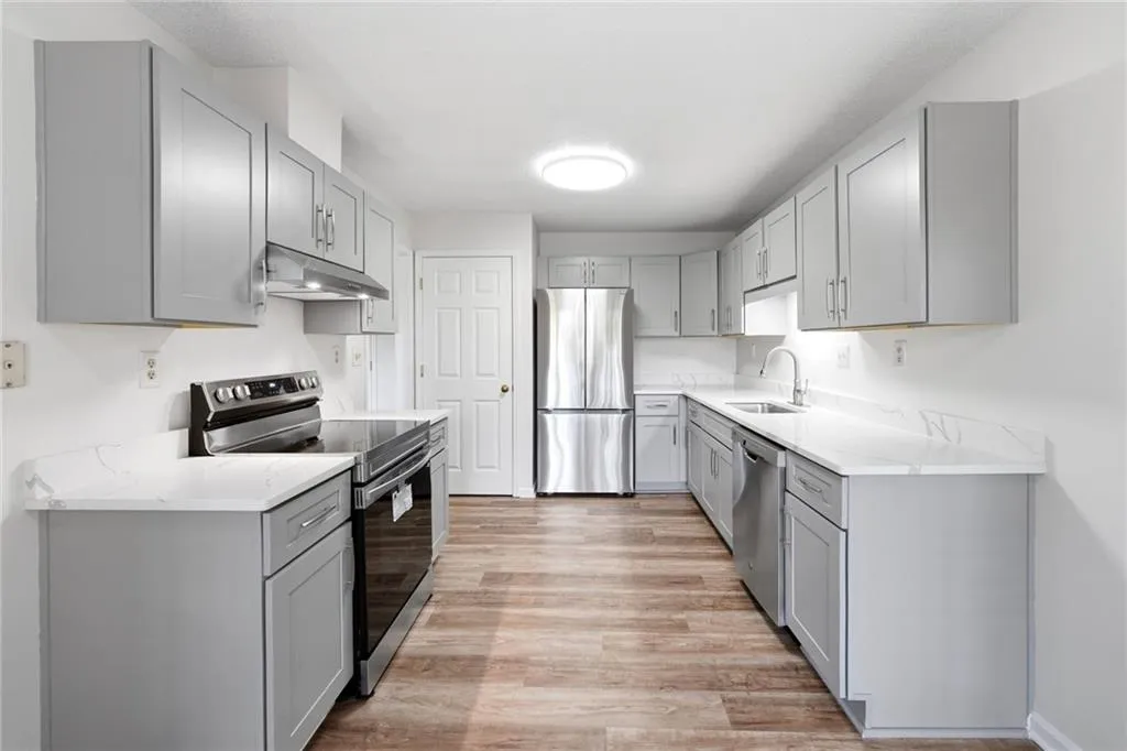 Kitchen featuring gray cabinetry, stainless steel appliances, light stone countertops, and light wood-type flooring