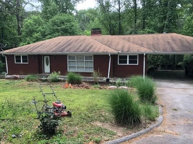 Ranch-style house featuring driveway, a chimney, a front lawn, and an attached carport