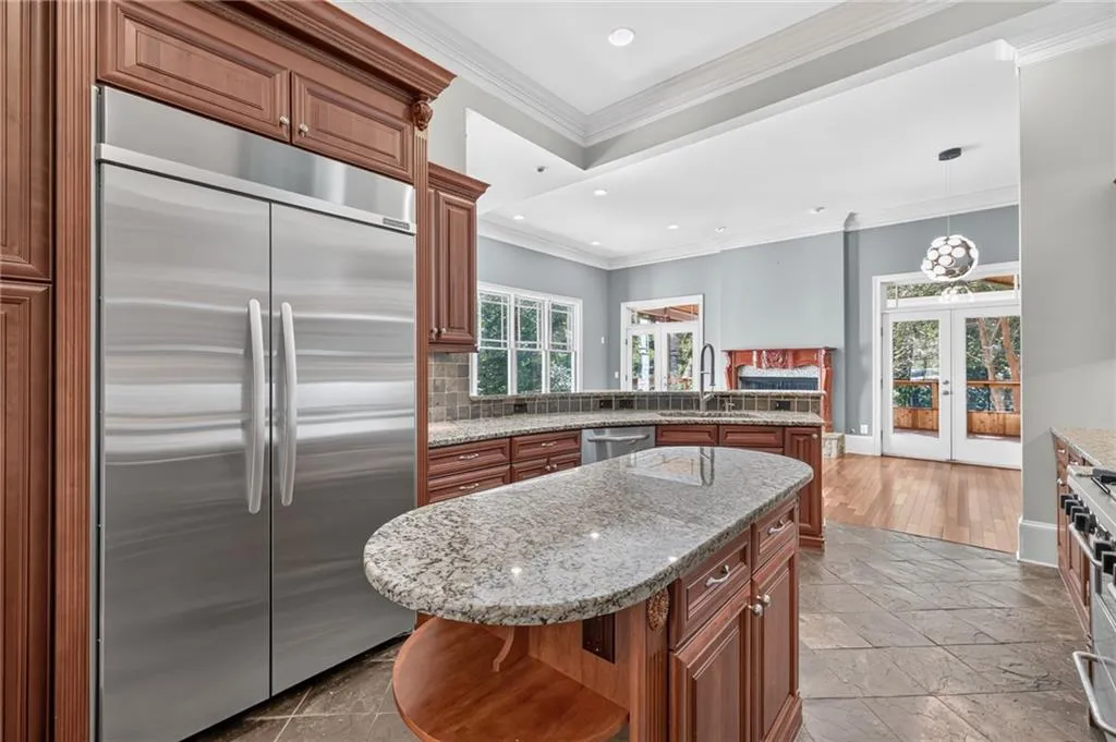 Kitchen featuring custom wood cabinetry, stainless steel panel-ready refrigerator, stone countertops, central island, and tiled flooring