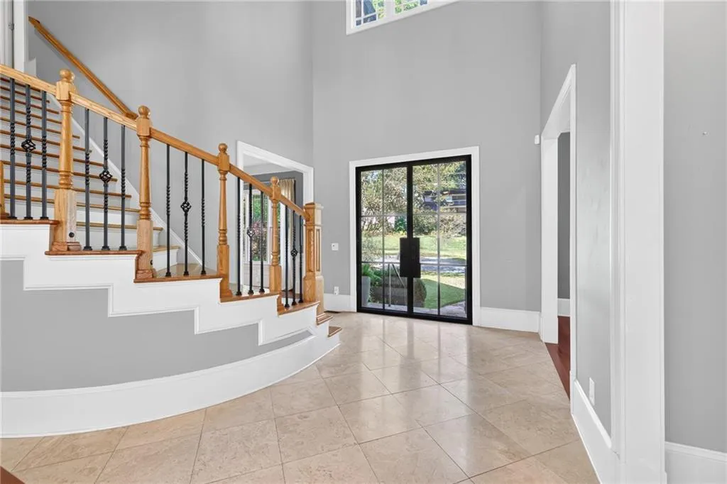 Grand foyer featuring high ceilings, double entry doors with black frames, tile flooring, and a curved staircase with wood railings and metal balusters