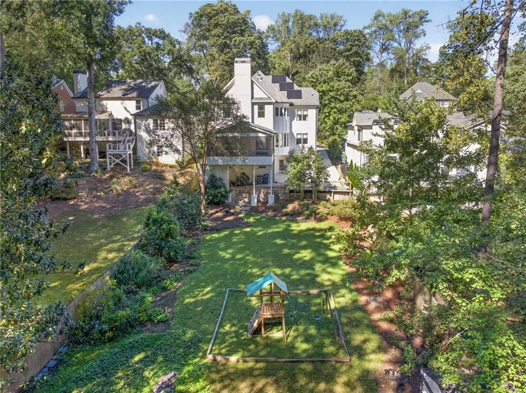 Expansive backyard featuring a manicured lawn, mature trees, and a ground-level stone patio
