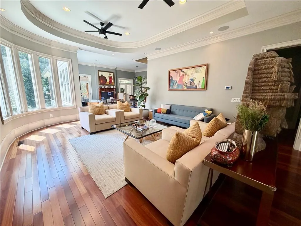 Sophisticated living space showcasing a curved architectural ceiling with integrated recessed lighting and ceiling fans, hardwood flooring throughout, generous seating arrangements with neutral upholstery, floor-to-ceiling windows with natural light exposure, and a cohesive open-concept layout with multiple zones for entertaining and relaxation