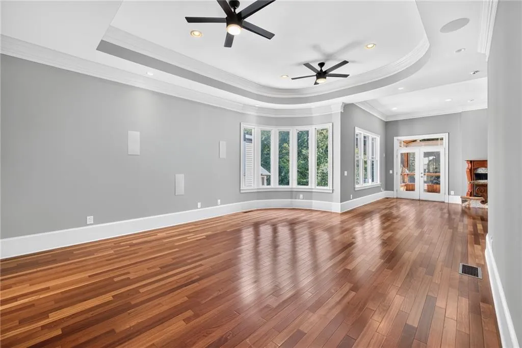 Tray ceiling with recessed lighting, wood-finish flooring, bay window, and dual ceiling fans