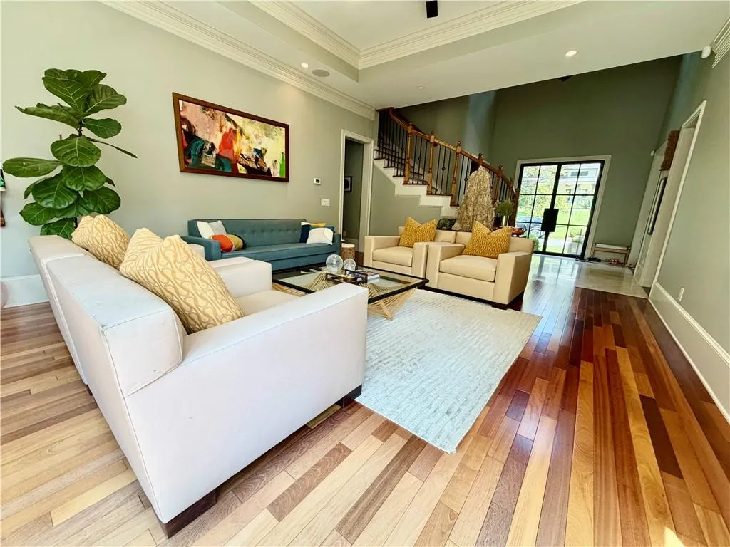 Multi-tonal wood-finish flooring, tray ceiling with recessed lighting, staircase with decorative metal balusters, and a large multi-pane glass-panel door