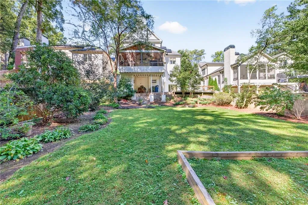 Expansive backyard featuring a manicured lawn, tiered wooden garden borders, mature trees, multi-level screened porches, and a masonry chimney