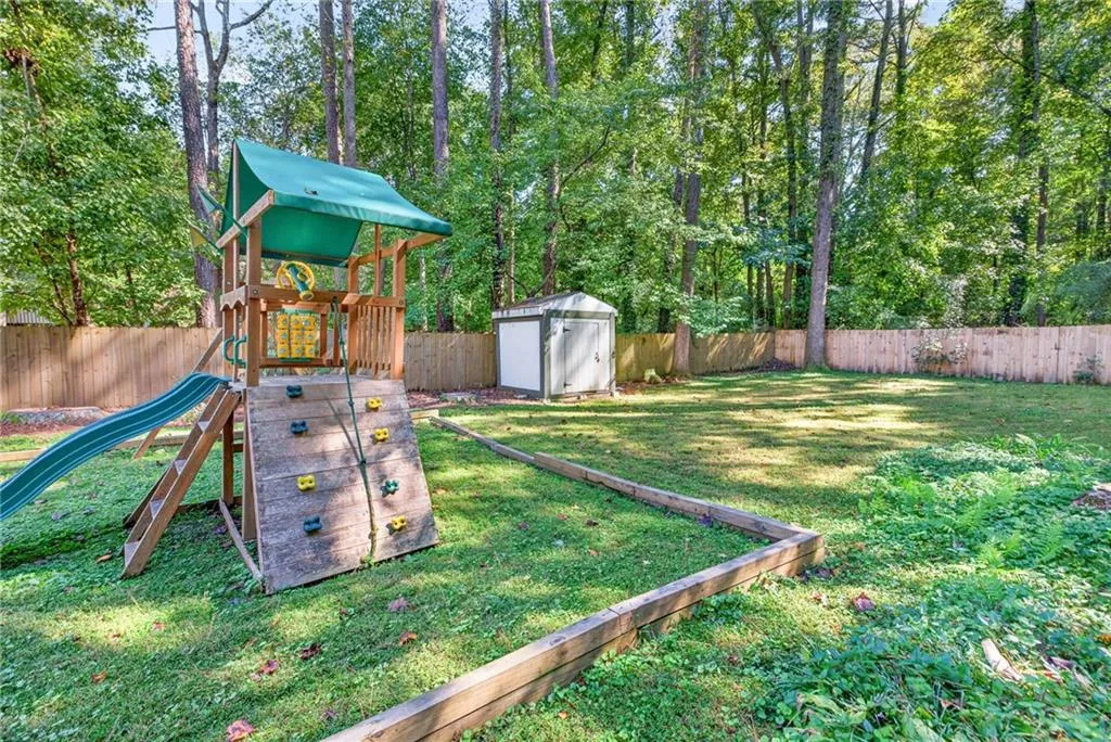 Expansive backyard featuring a fenced perimeter, wood-frame storage structure, and mature tree line