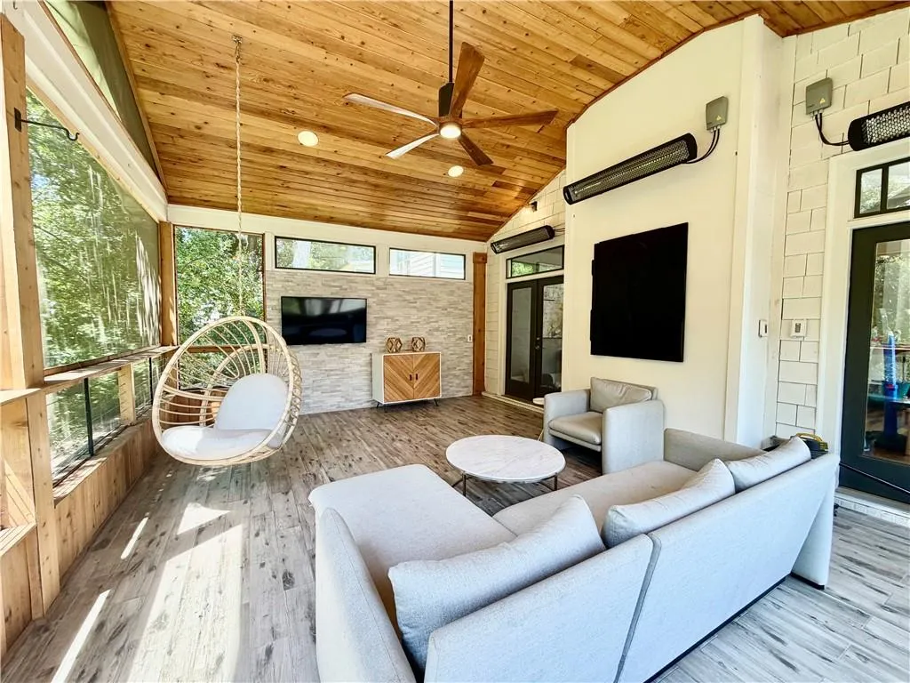 Screened-in porch featuring a natural wood-plank vaulted ceiling, wood-finish flooring, a stone-veneer wall, and mounted infrared heaters