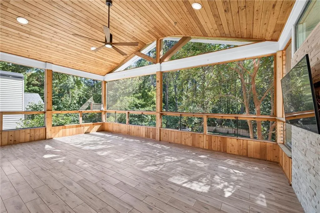 Screened-in porch featuring a vaulted wood-plank ceiling, wood-finish flooring, full-height window screening, stone-cladding fireplace surround, and recessed lighting