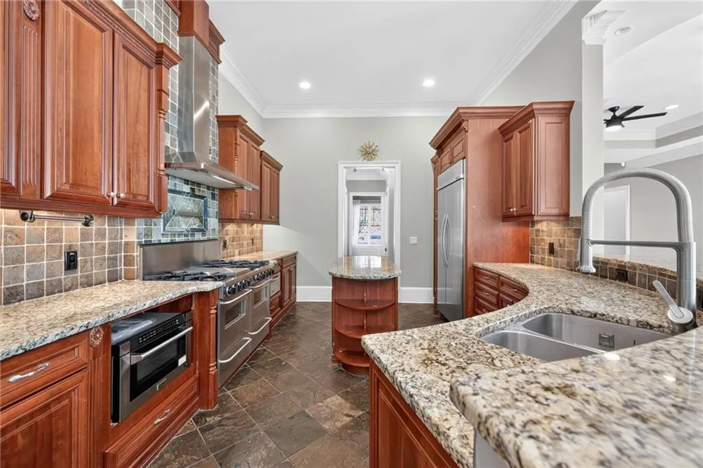 Chef's kitchen featuring rich wood cabinetry, stainless steel appliances including a professional-style range, granite countertops, a tile backsplash, and an oversized island with seating