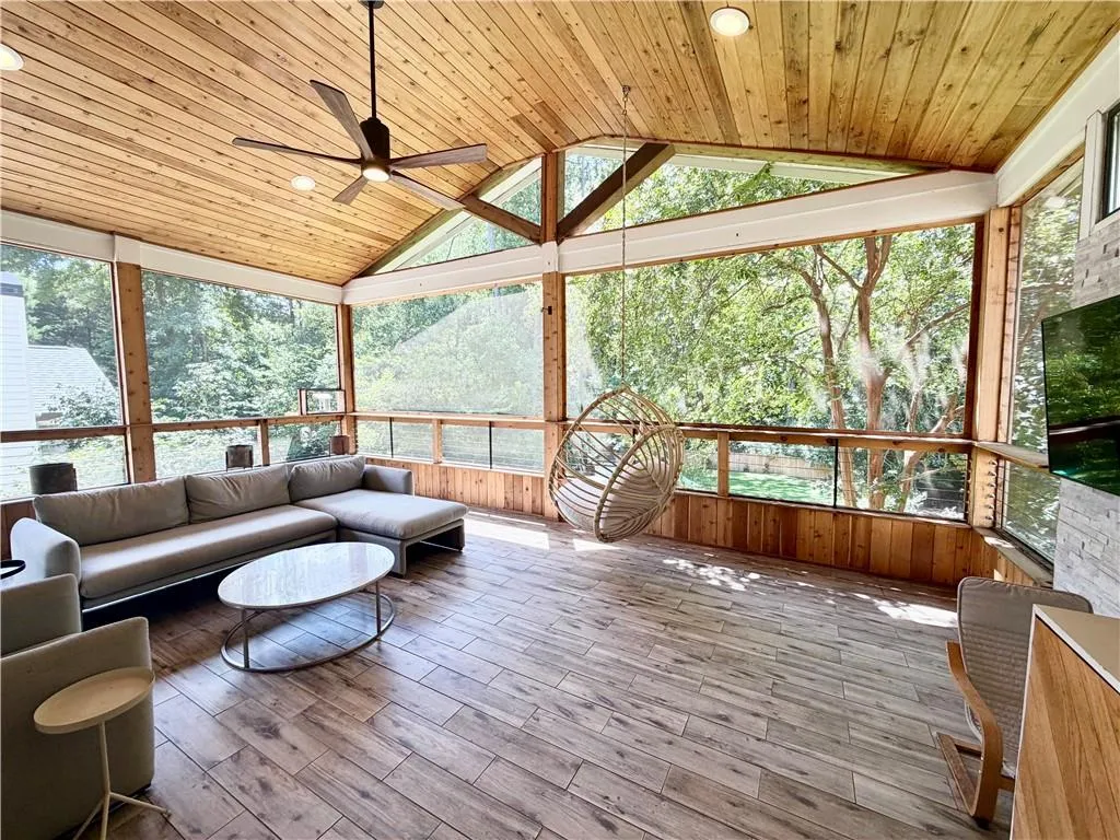 Screened porch featuring a vaulted wood-plank ceiling, wood-finish tile flooring, a mounted ceiling fan, and a floor-to-ceiling stone-clad fireplace
