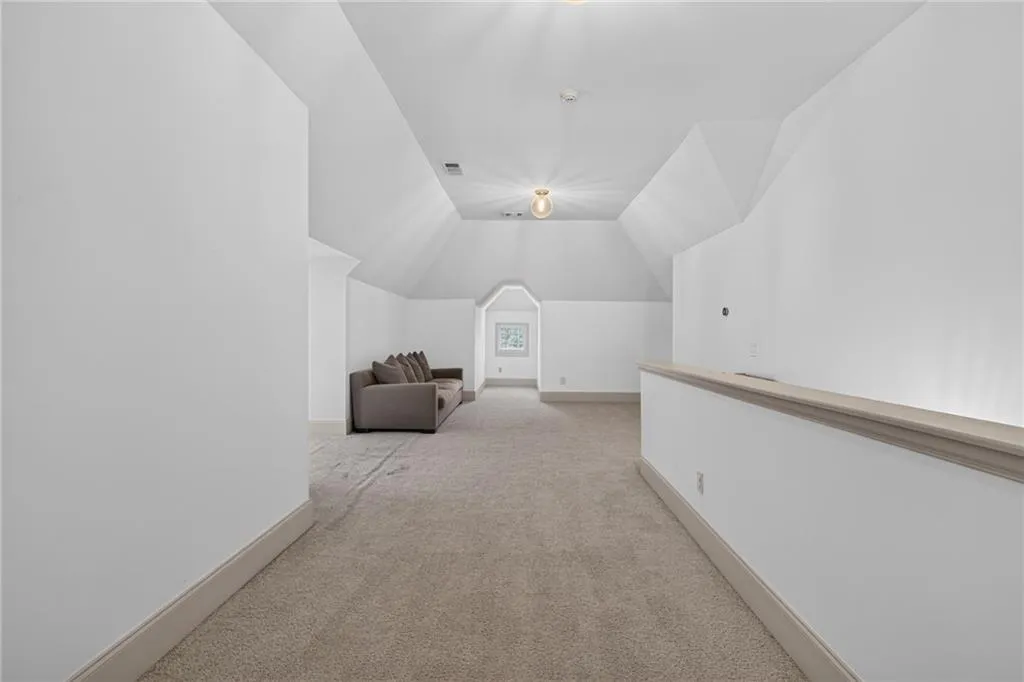 Expansive interior space featuring vaulted ceilings, neutral carpeting, and a built-in wall partition with a flat ledge