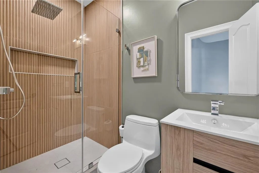 Walk-in shower with vertical-slat textured tile surround, recessed wall niche, and rainfall showerhead, paired with a modern wood-finish vanity featuring an integrated sink and rectangular mirror
