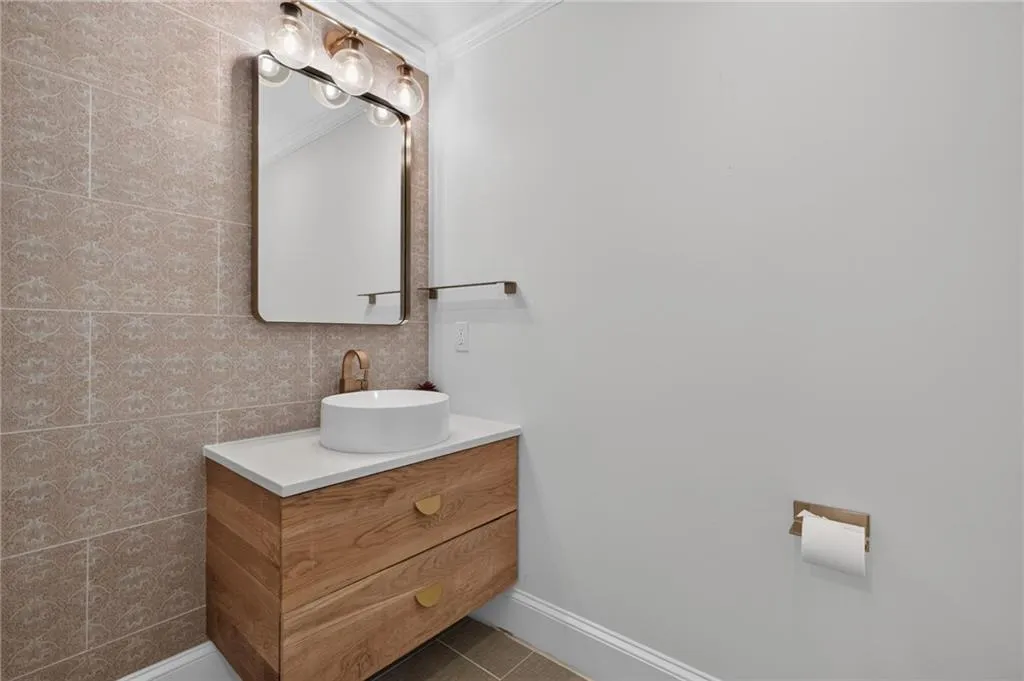 Floating wood-finish vanity featuring a white vessel sink, quartz countertop, metallic hardware, and a patterned tiled accent wall