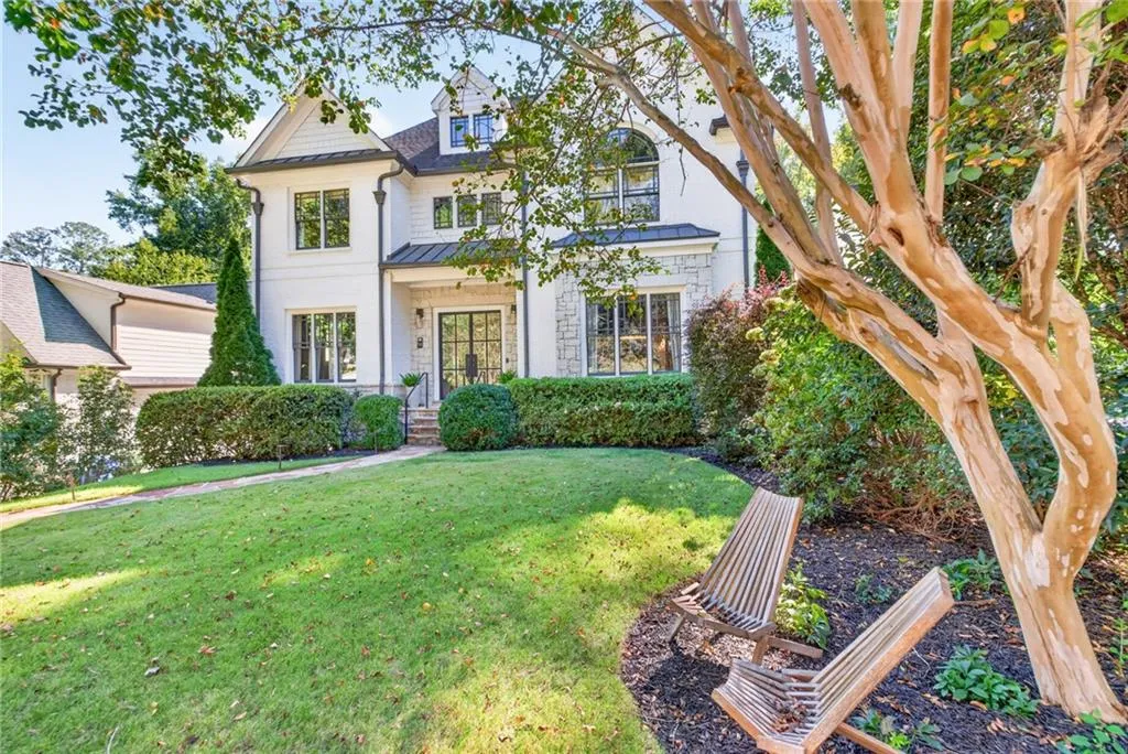 Two-story exterior featuring white siding, stone veneer accents, multi-pane windows, a metal-accented roofline, and a manicured front lawn