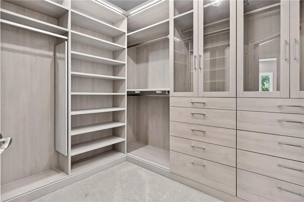 Custom walk-in closet featuring light-toned wood-finish cabinetry, built-in shelving, glass-front upper storage, soft-close drawers, and brushed metal hardware