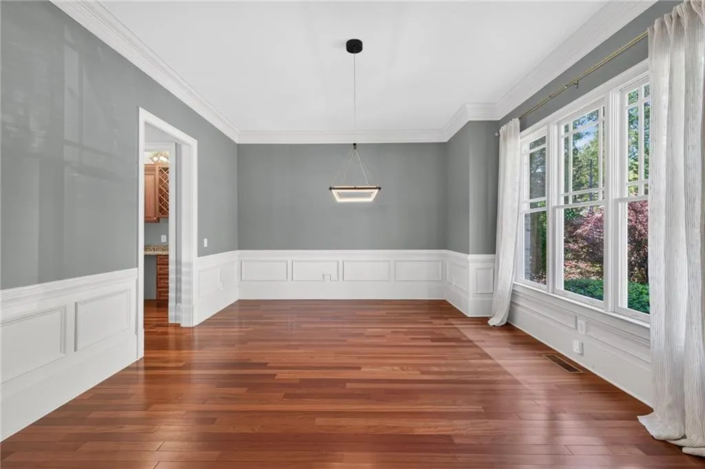 Elegant dining room showcasing rich hardwood flooring, crisp white wainscoting with detailed panel work, and soft gray upper walls