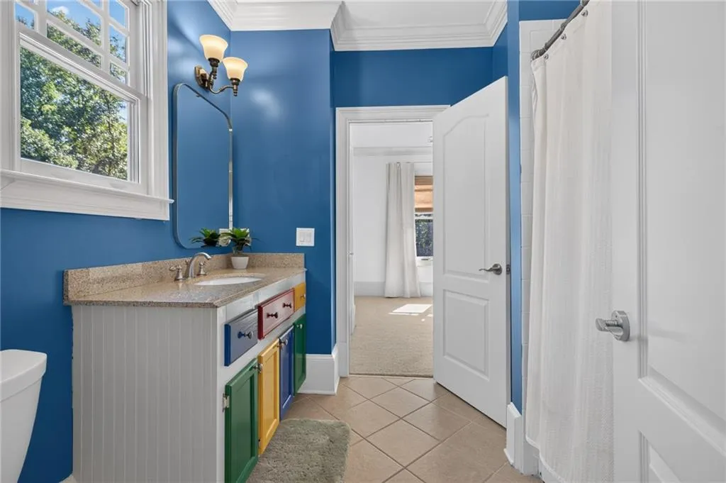 Bathroom featuring a stone-top vanity with multi-colored cabinetry, tile flooring, crown molding, and a wall-mounted light fixture above a rectangular mirror
