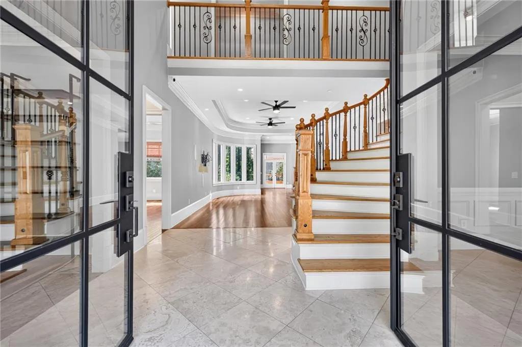 Grand foyer featuring large metal-framed glass doors, a curved staircase with wood treads and ornate balusters, polished tile flooring, wood-finish flooring, and a two-story ceiling with recessed lighting