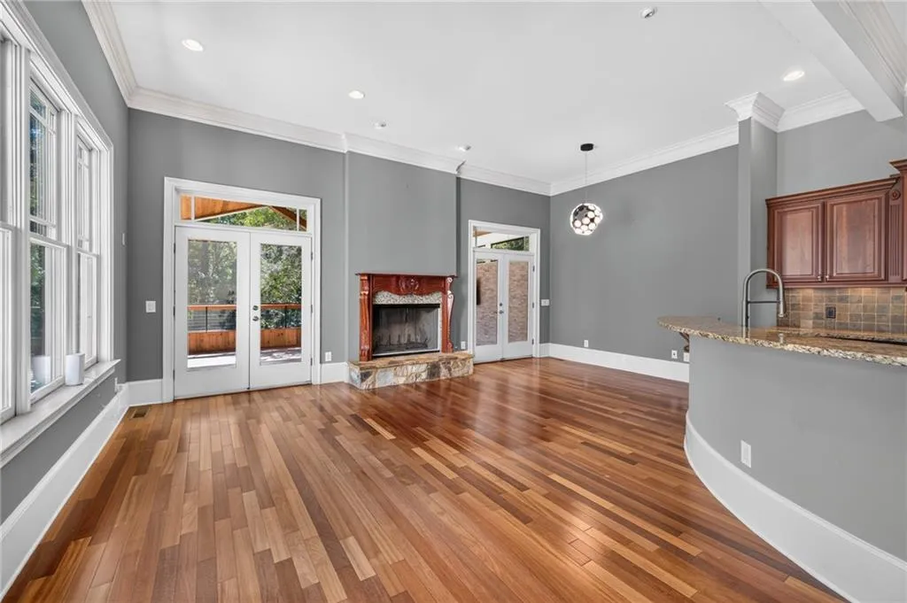 Open-concept area featuring wood-finish flooring, a fireplace with a stone hearth and wood mantel, crown molding, double glass-paneled exterior doors, and a curved breakfast bar with a stone countertop