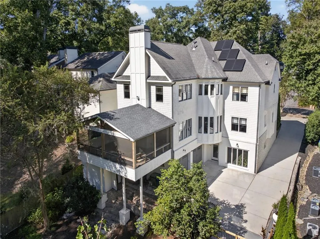 Multi-story residence featuring shingle and vertical panel siding, an elevated screened porch, a paved driveway, and roof-mounted solar panels